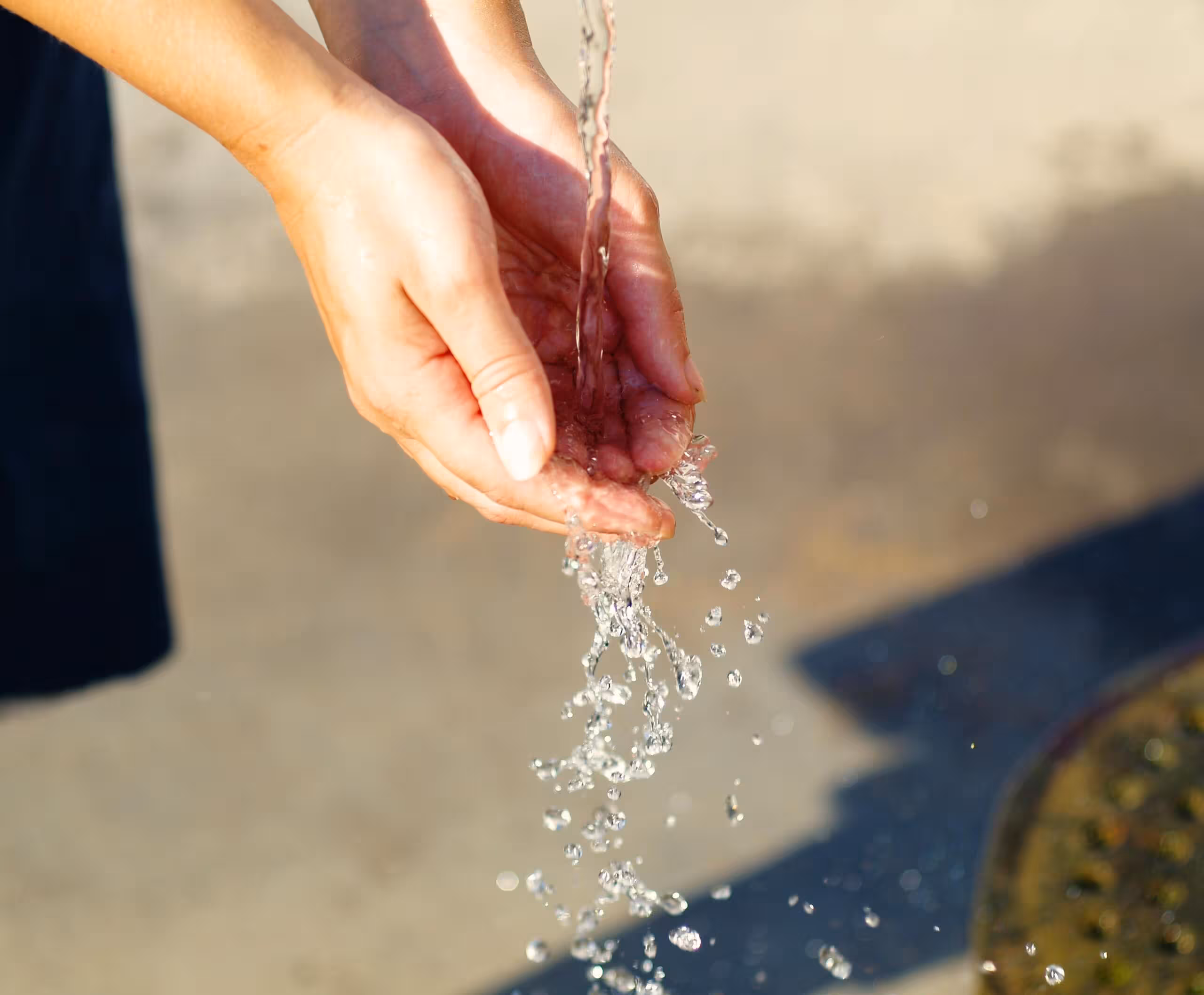 Two hands cupped to catch a stream of water; the water is dripping of their fingers