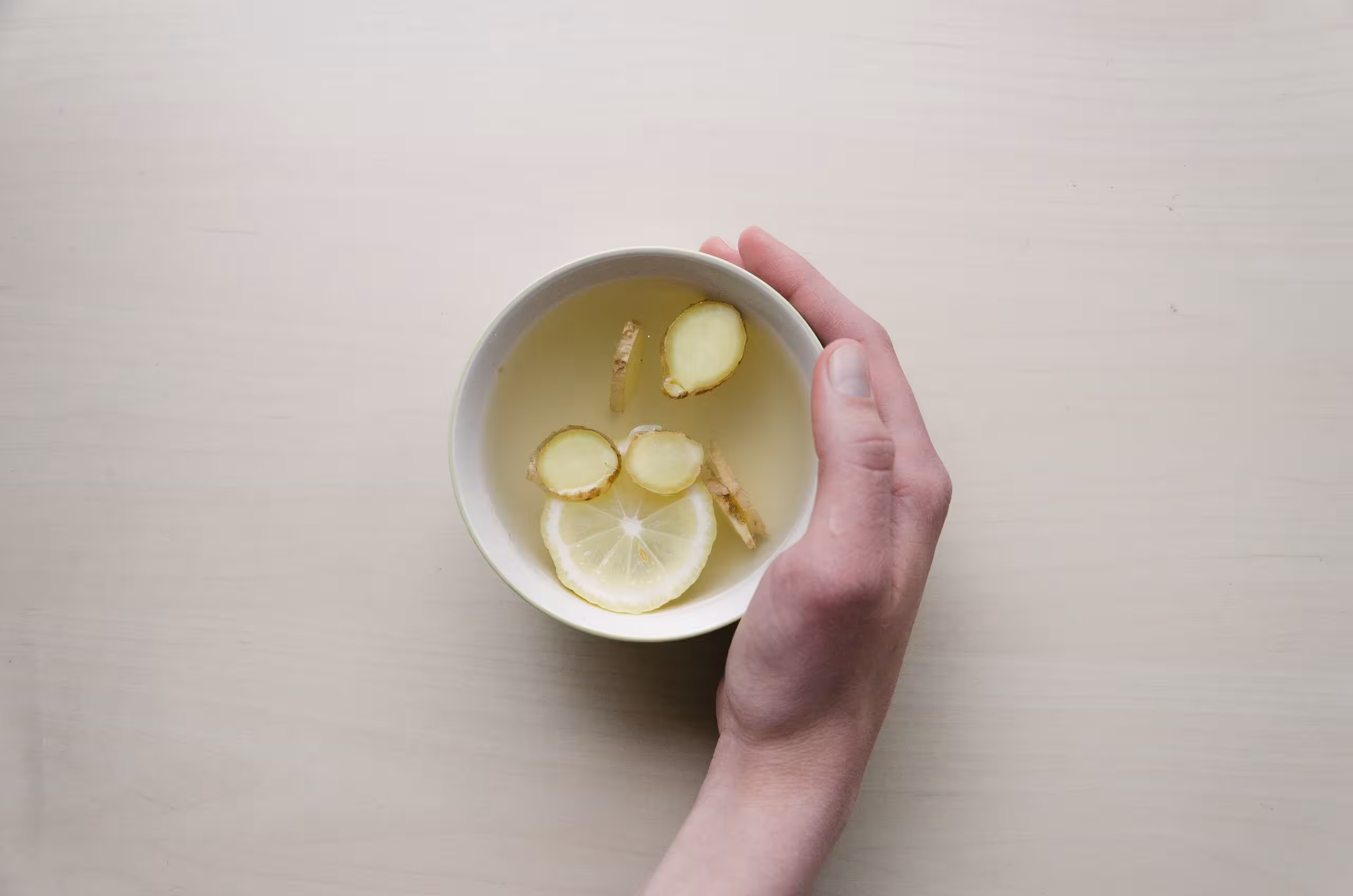 A hand holding a cup of water with pieces of ginger and lemon in it; ginger is good for nausea