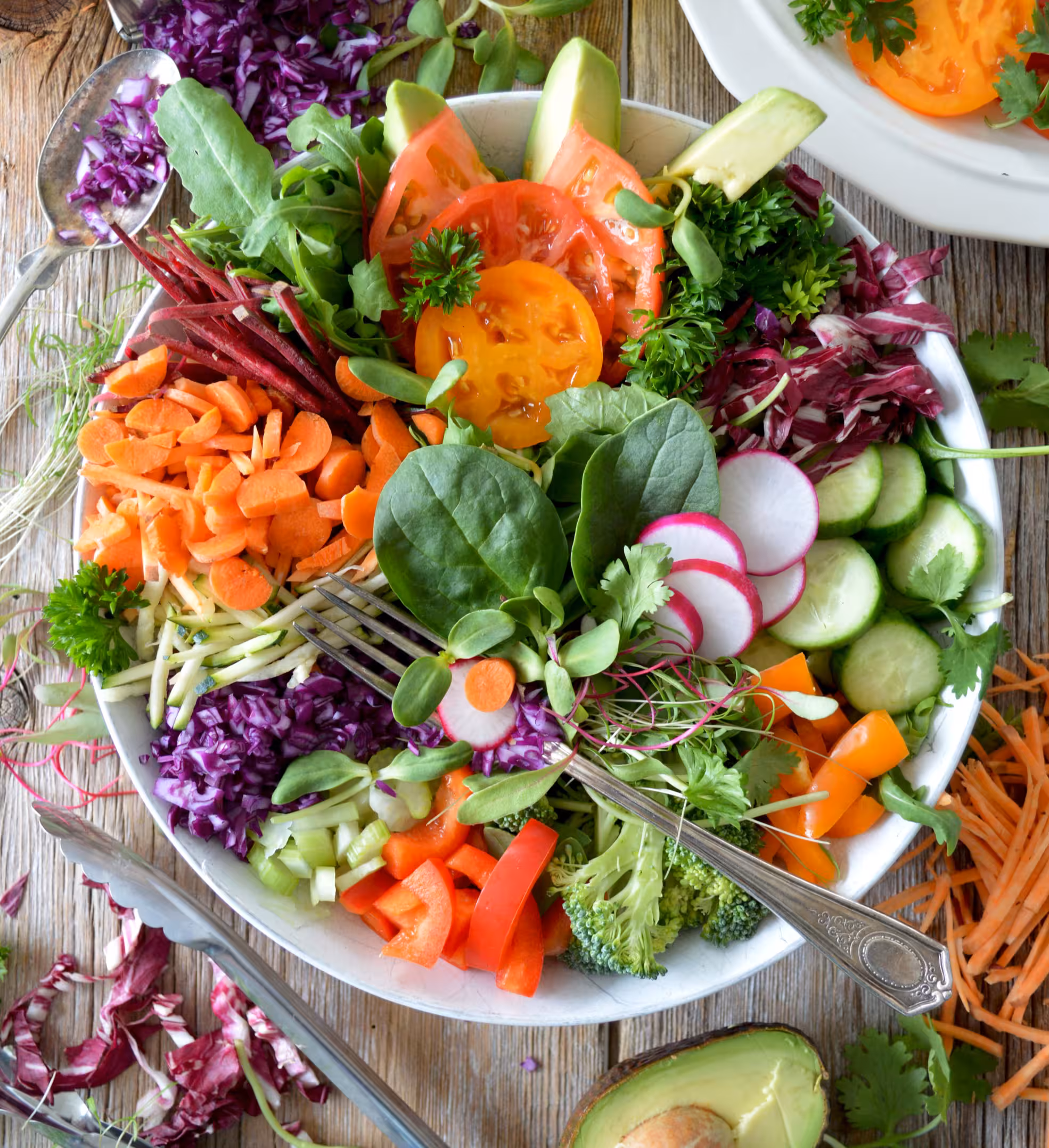 A bowl filled with different coloured vegetables and herbs and other vegetables surrounding the bowl