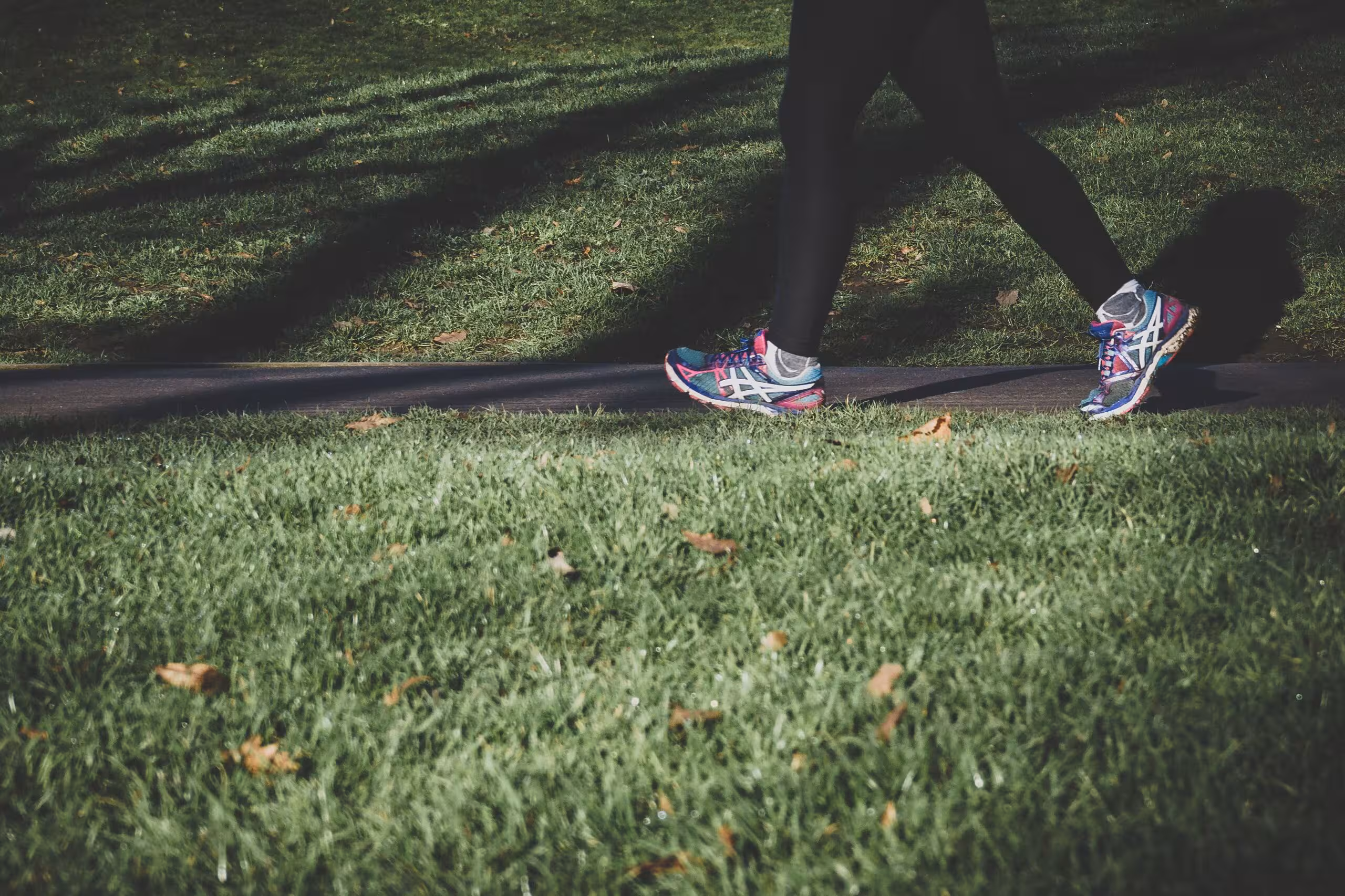 Picture of women's legs in black pants and running shoes walking on a grass surrounded path