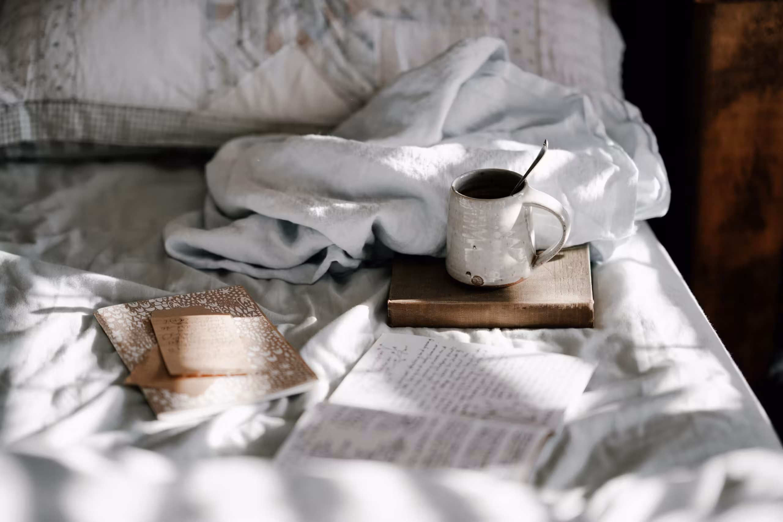 unmade bed with books and a mug 