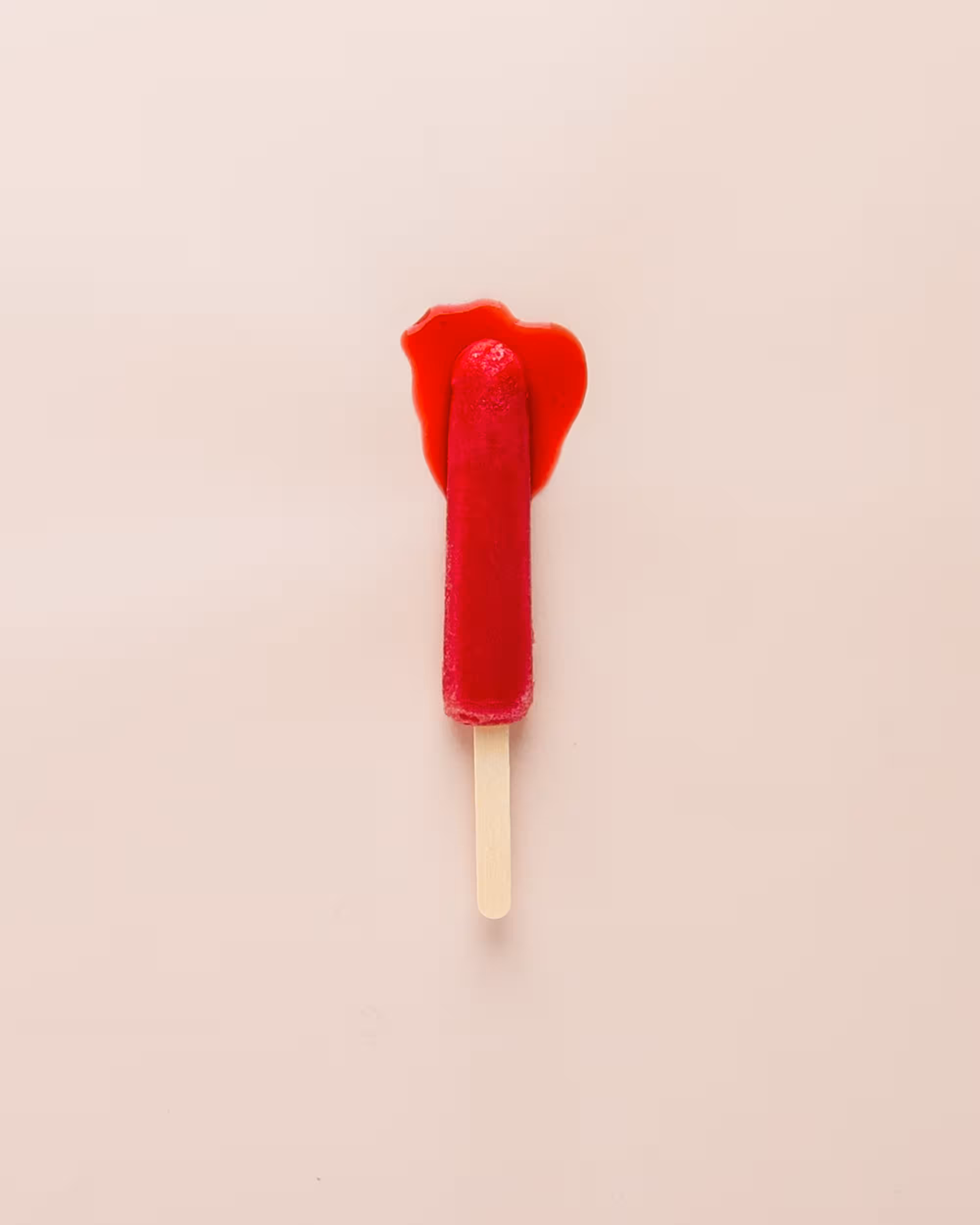 a red popsicle that is starting to melt at the top against a peach background