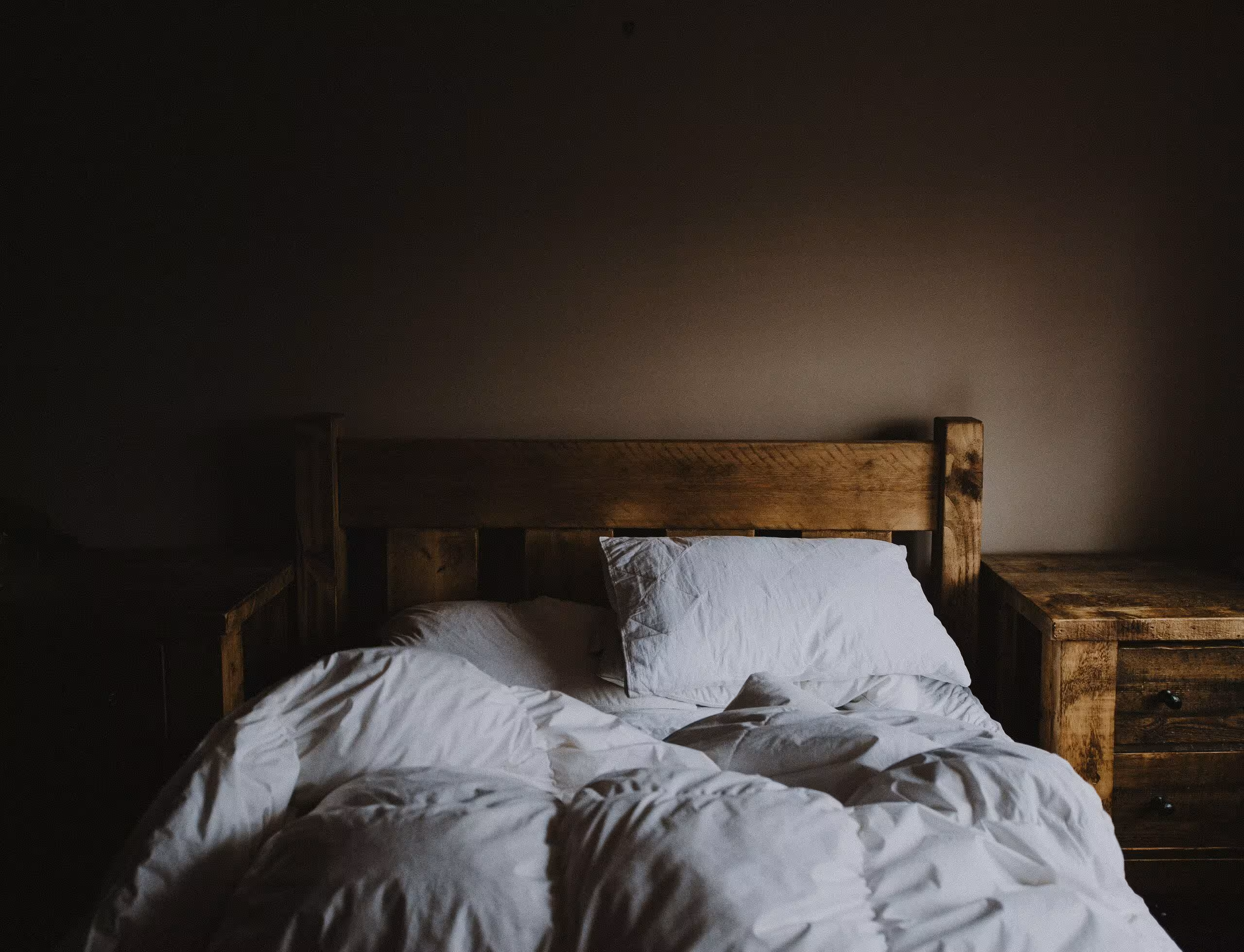 An unmade bed with white sheets and duvet and the room is dark